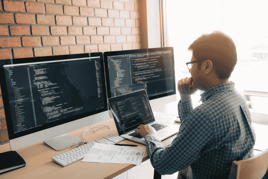 Programador trabalhando com múltiplas telas exibindo código-fonte em Python, em ambiente de desenvolvimento.