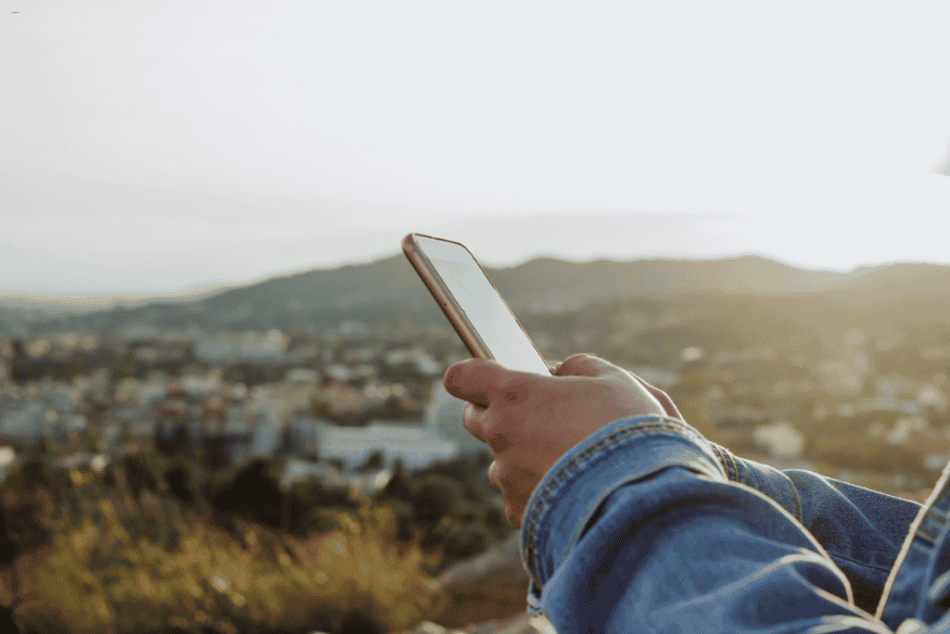 Pessoa usando smartphone em área rural com vista panorâmica de fundo