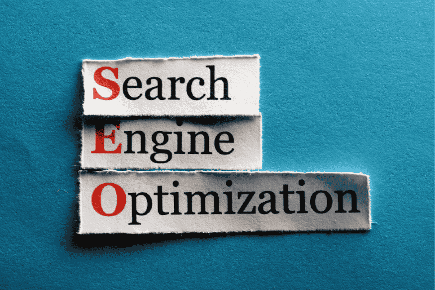 Termo SEO em destaque sobre recortes de papel com as palavras Search, Engine e Optimization.