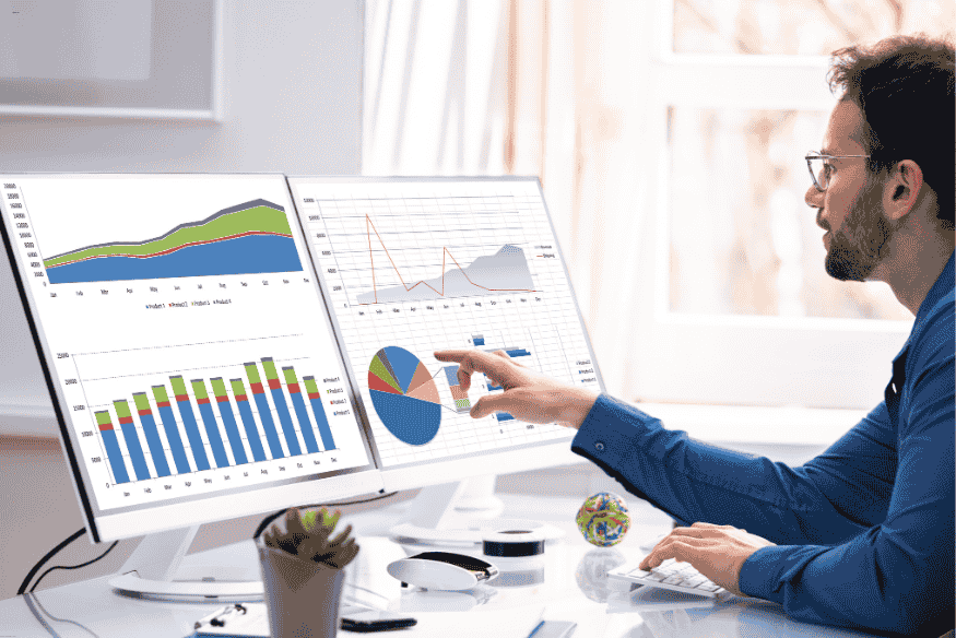 Profissional analisando gráficos em dois monitores com dados de desempenho e métricas de marketing.