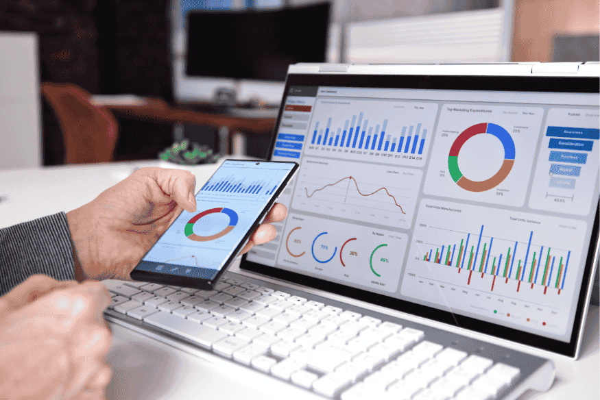 Pessoa comparando gráficos de desempenho em smartphone e notebook com dashboards completos.