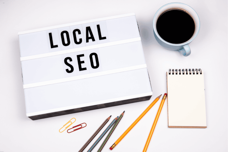 Letreiro com as palavras "Local SEO" ao lado de caderno, café e lápis sobre a mesa, simbolizando estratégias de SEO local.