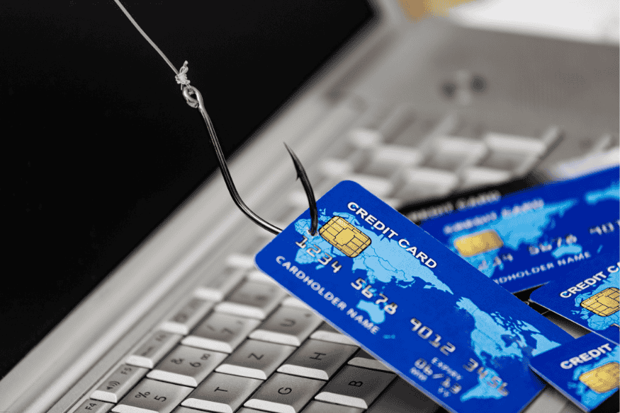 Cartão de crédito fisgado por anzol sobre teclado de notebook, simbolizando golpe.