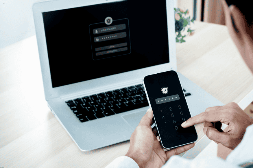 Usuário inserindo código numérico no celular com tela de login exibida no notebook.