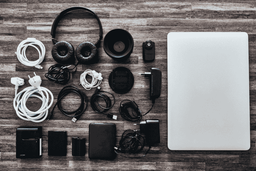 Acessórios de tecnologia organizados ao lado de notebook sobre superfície de madeira