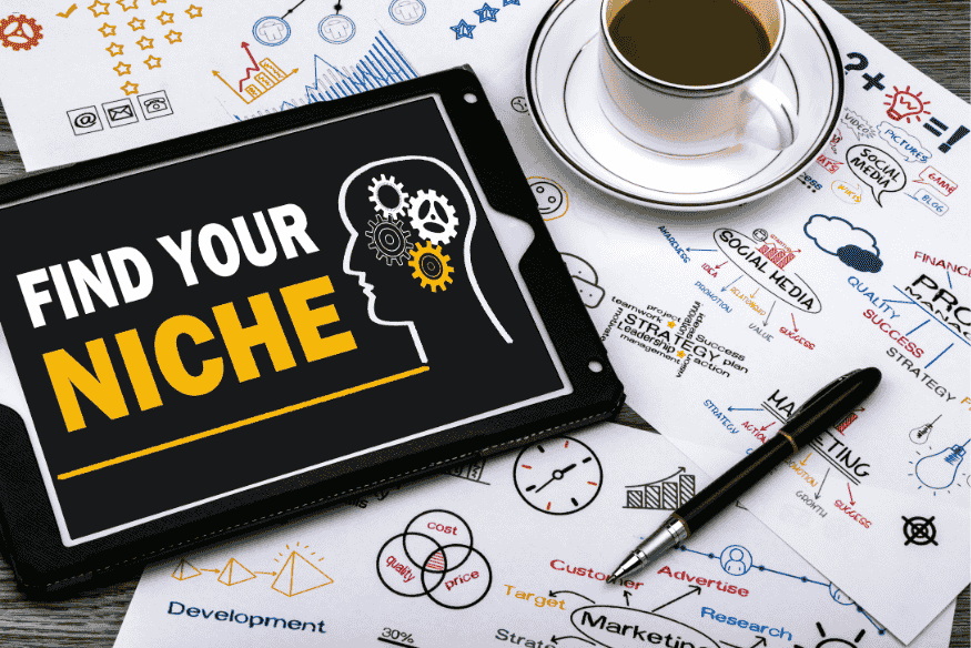 Tablet com a frase "Find your niche" sobre mesa com anotações de marketing e uma xícara de café.