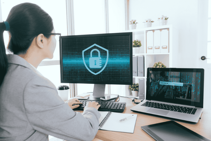 Mulher trabalhando em dois monitores com tela de segurança e autenticação digital.