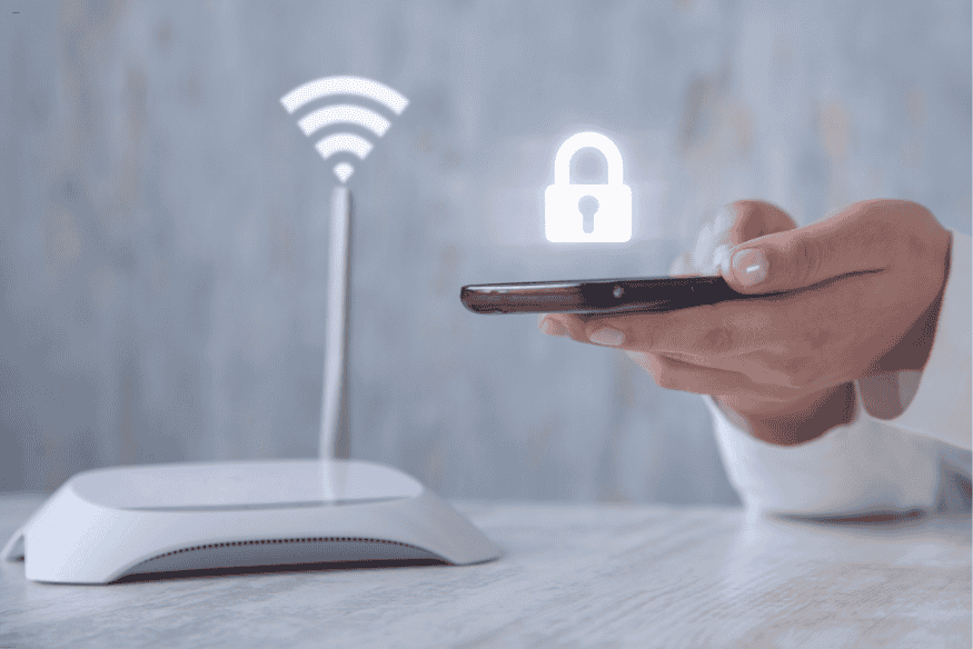 Pessoa segurando smartphone com ícone de cadeado conectado a roteador Wi-Fi, representando segurança de rede doméstica.