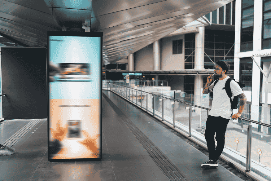 Homem observa painel de publicidade digital em local público com tecnologia interativa.
