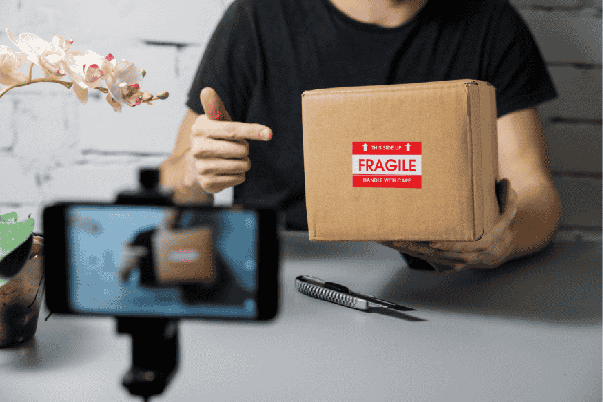 Criador de conteúdo gravando unboxing de produto com smartphone e caixa rotulada como frágil.