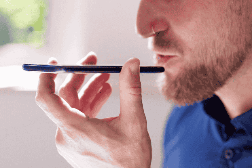 Homem falando próximo ao smartphone, utilizando comando de voz para pesquisar na internet.